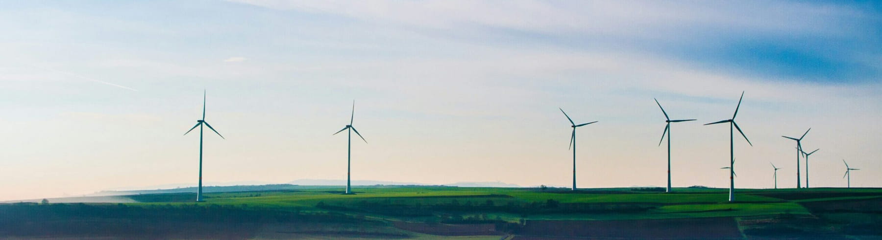 Wind turbines stand on a green, rolling landscape under a blue sky, generating renewable energy in the countryside.