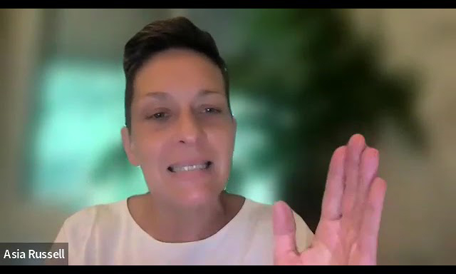 A person with short hair and a white shirt raises their hand while speaking during a video call. The name Asia Russell appears in the bottom left corner. The background is blurred.